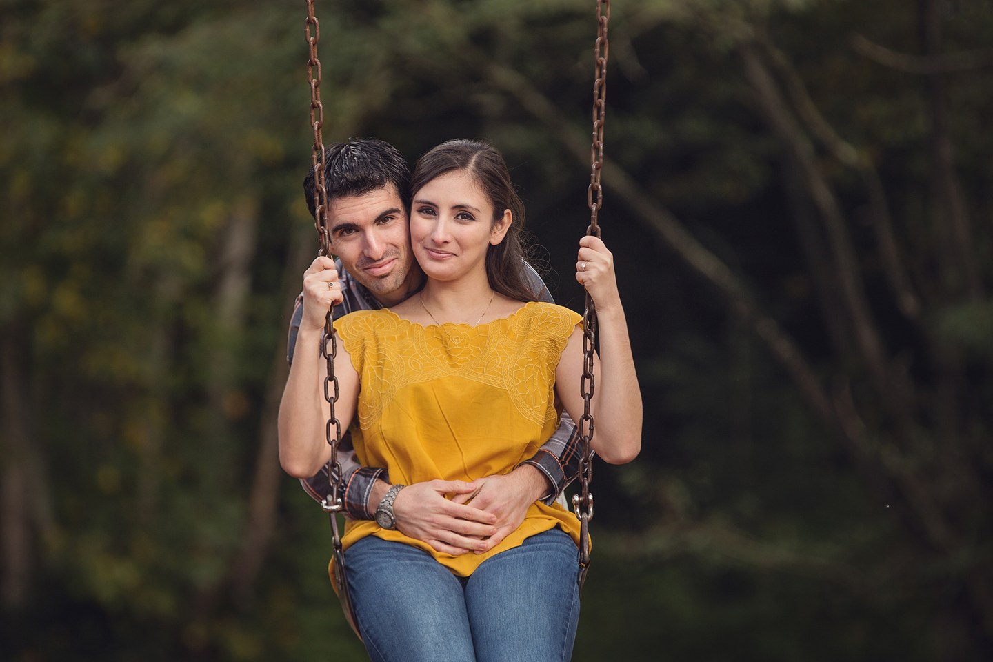 Pareja sentada junta en un columpio durante una sesión al aire libre.