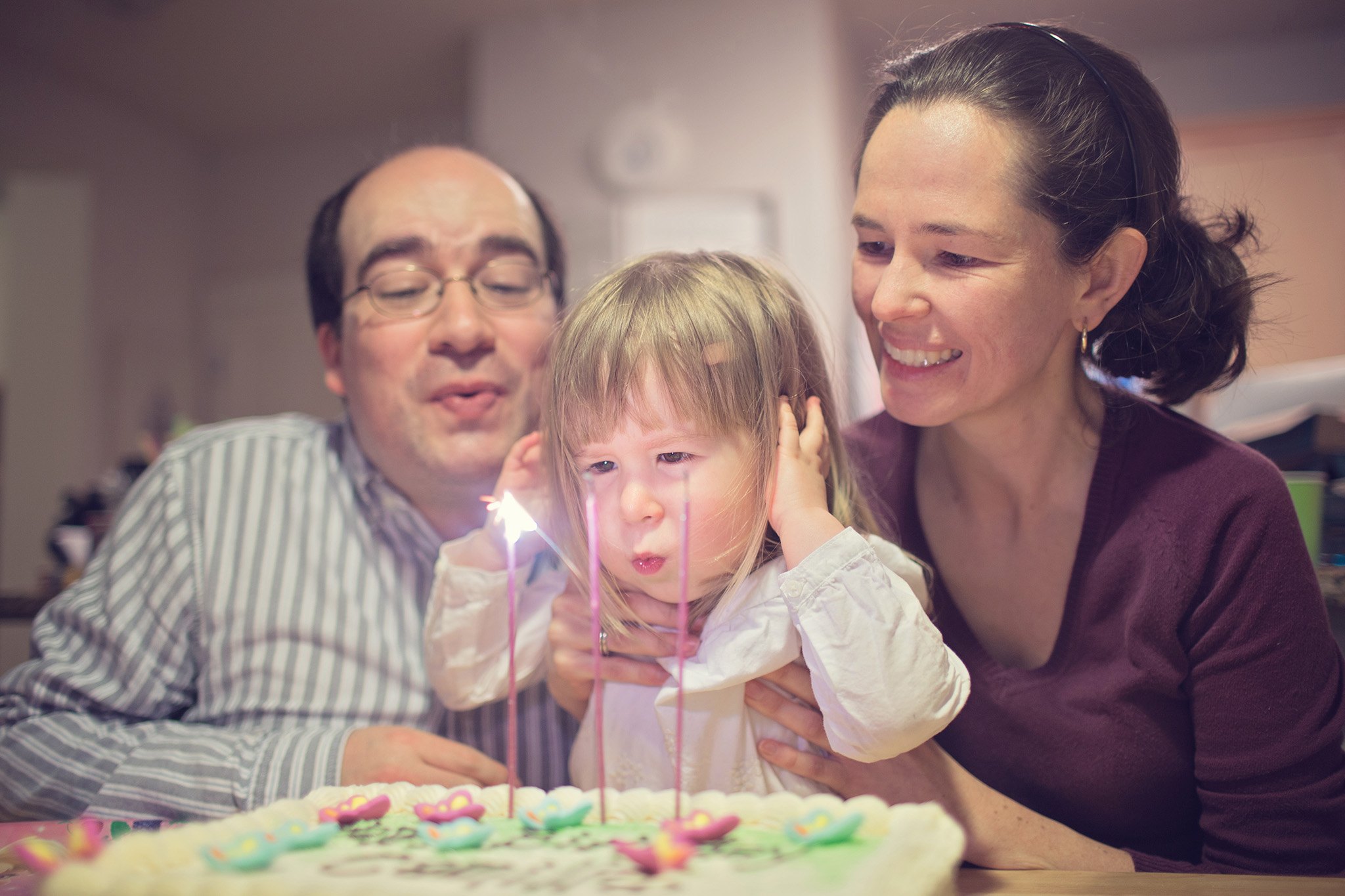 Familia reunida alrededor de una niña que apaga las velas de una torta.