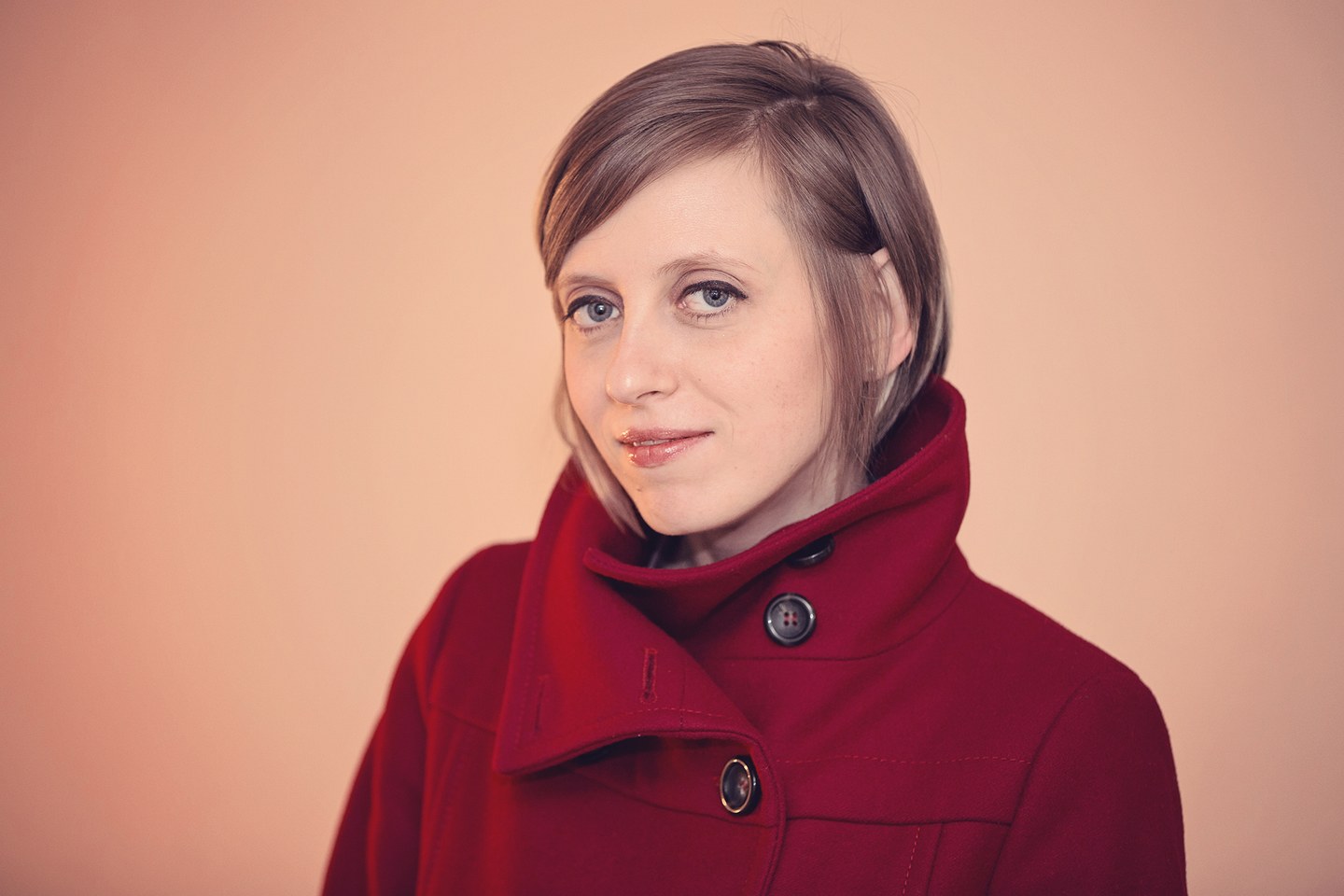 Retrato dirigido de una persona con abrigo rojo sobre un fondo cálido.