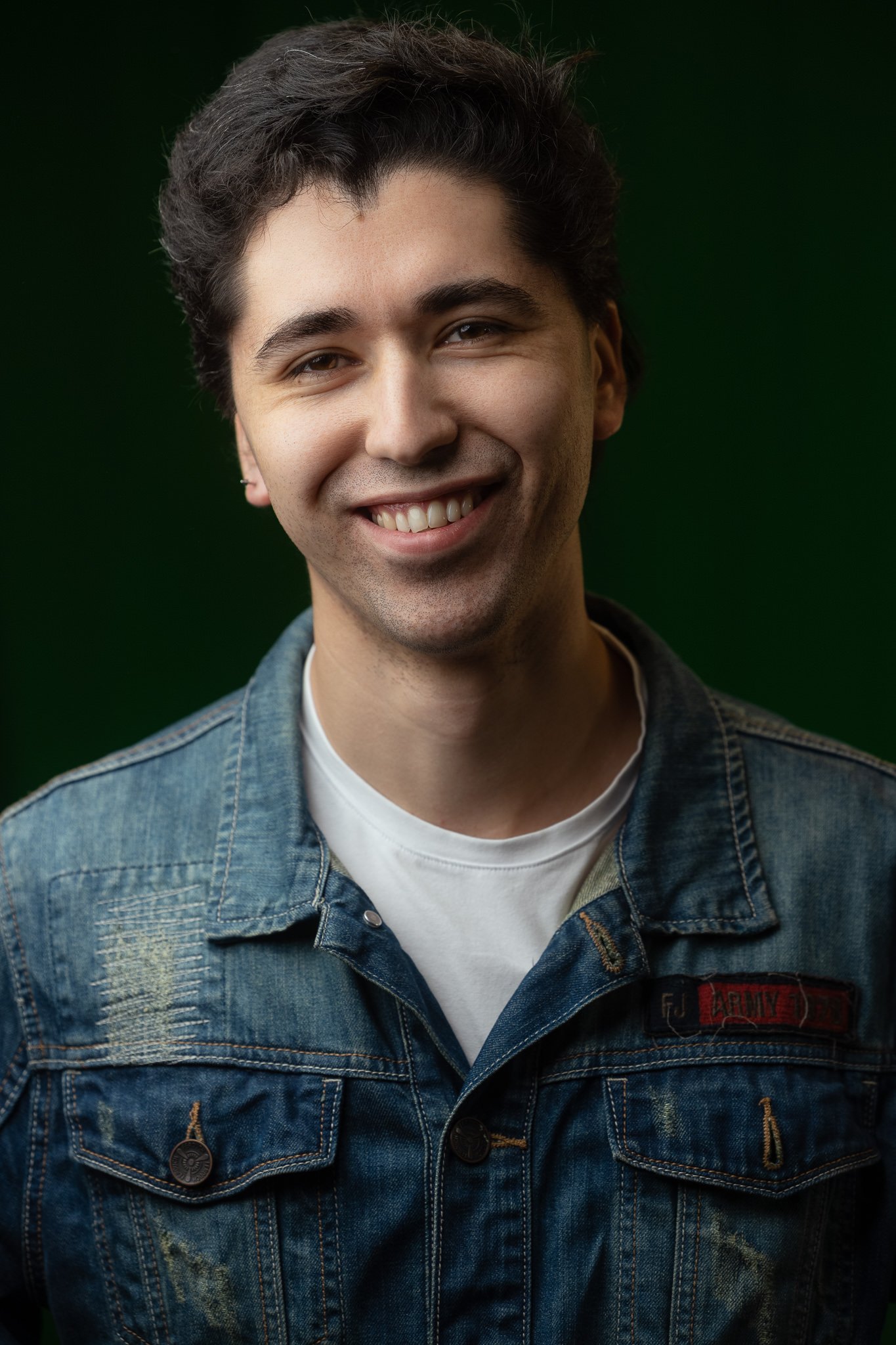 Retrato vertical de una persona sonriente con chaqueta de mezclilla sobre un fondo verde.
